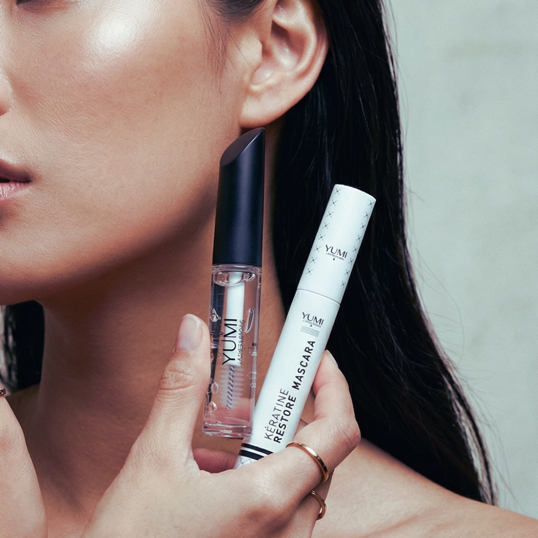 Woman holding YUMI Aftercare mascara and YUMI Keratin Mascara with a neutral background