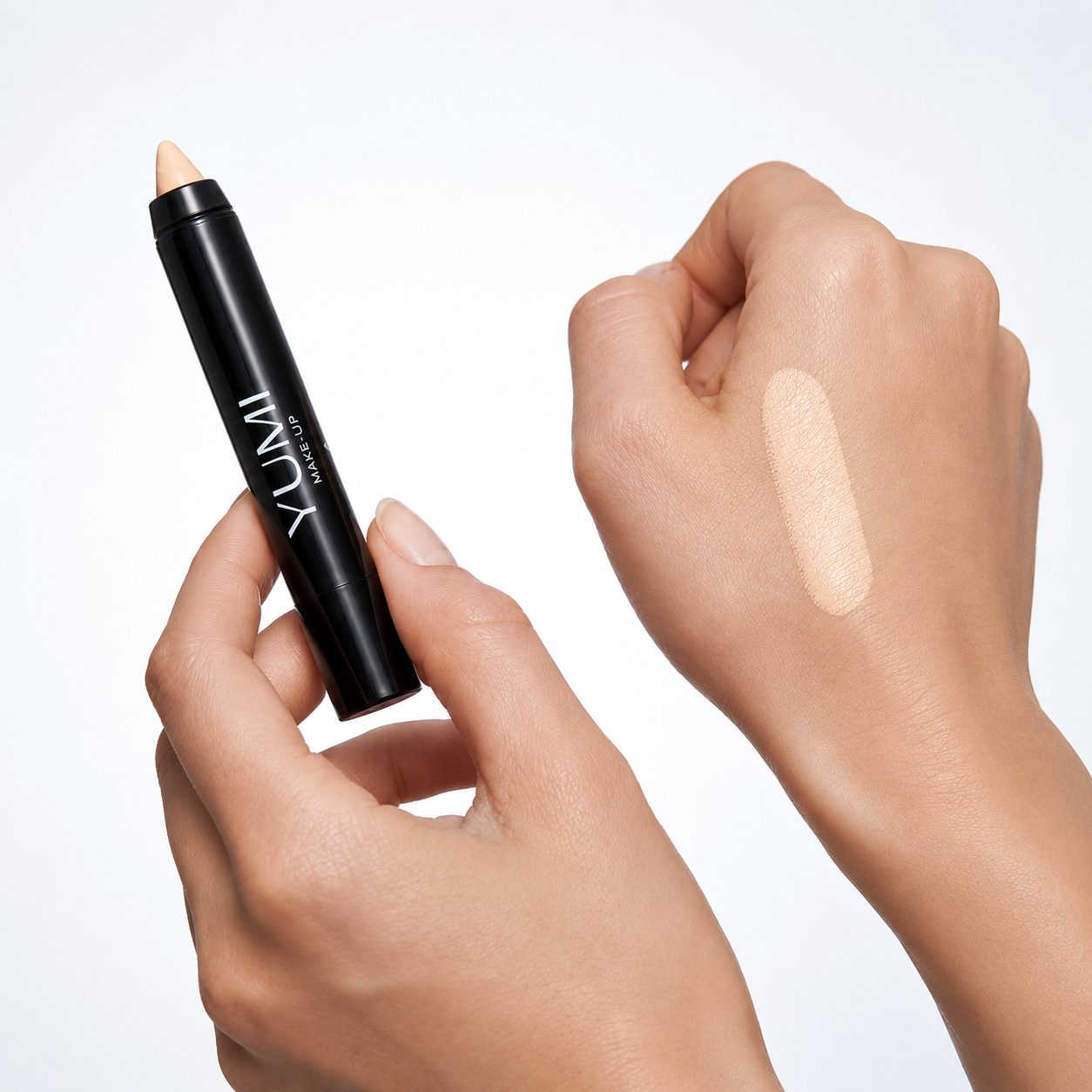 A black Yumii makeup stick with a light beige cream product, held by a hand next to a hand swatch showing the cream's texture and shade.